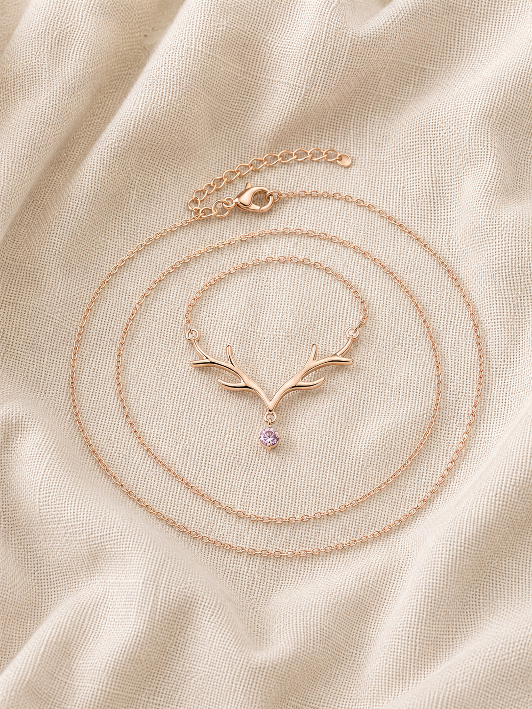 Dainty Rose Gold Antler Necklace with pink crystal drop displayed on cream linen fabric